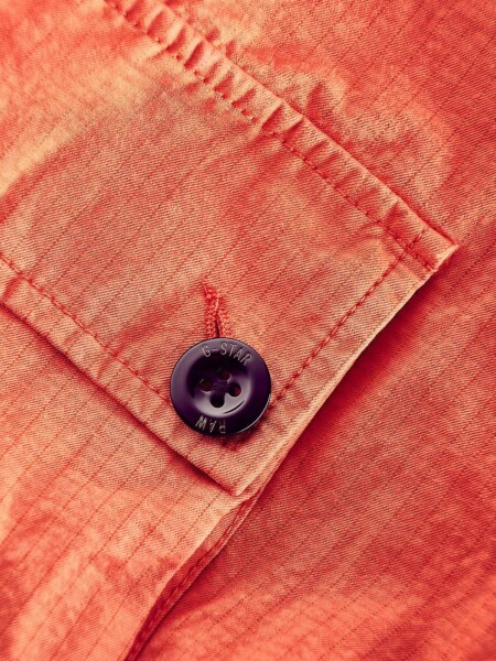 Detailfoto Knopf an orangener Jacke.